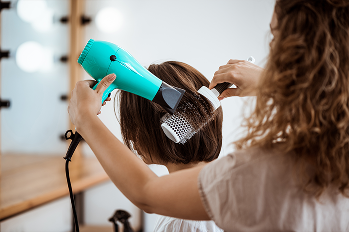 Uma mulher escova o cabelo de sua cliente num salão de beleza